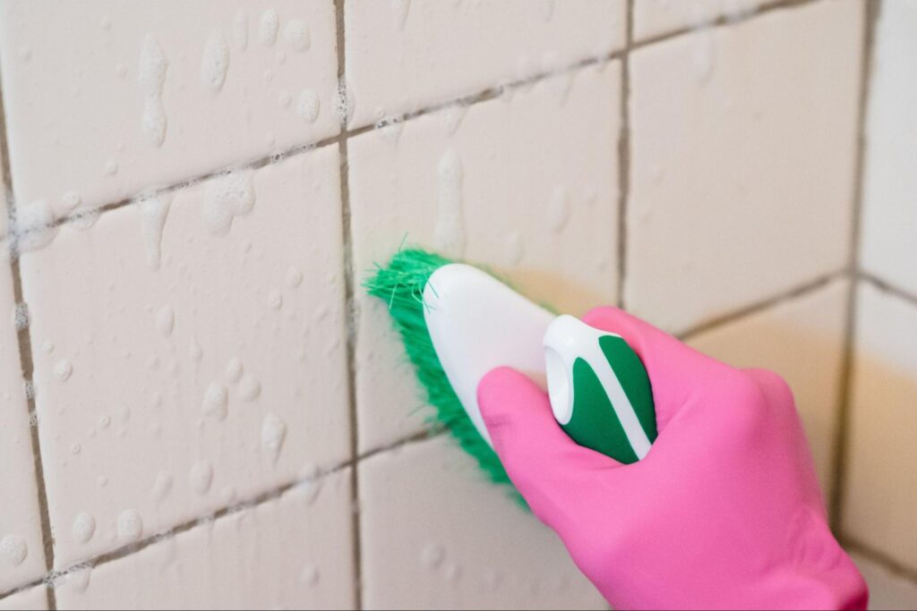 Gloved hand scrubbing bathroom grout during a deep clean.