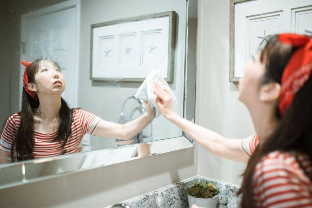 Woman cleaning a bathroom mirror during a regular home cleaning routine.